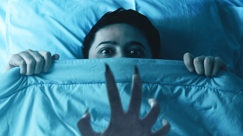 Person in bed scared looking at demon hand 