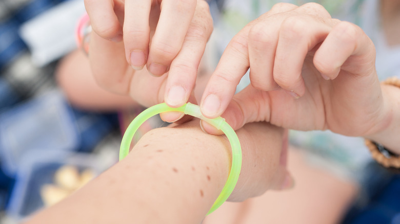 Someone putting a glow stick on another person's wrist covered in moles