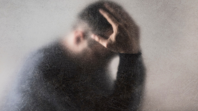 Man sitting with head in hands behind fogged glass 