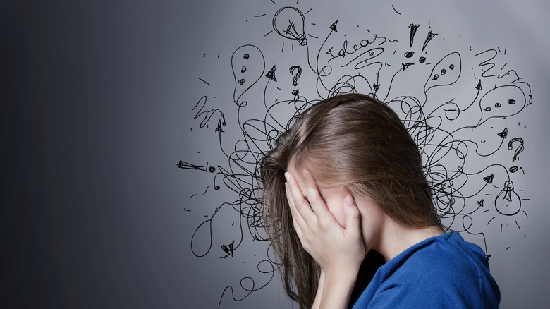 woman holding face in hands with chaotic scribbles on the wall behind her