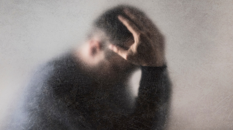 foggy image of man holding his head in distress