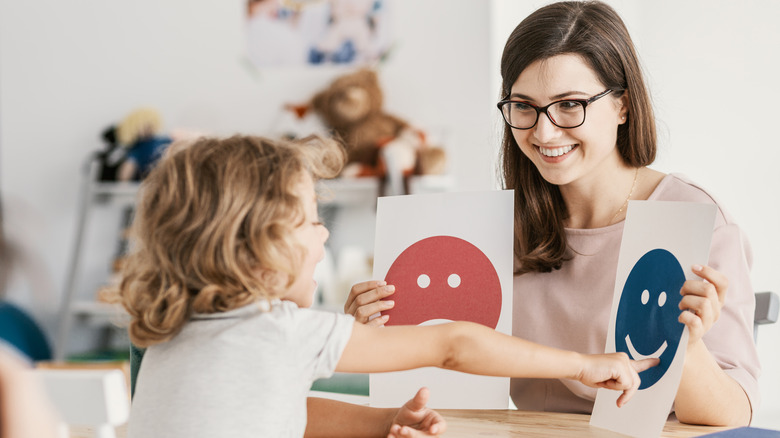 child points to smiley face card woman is holding