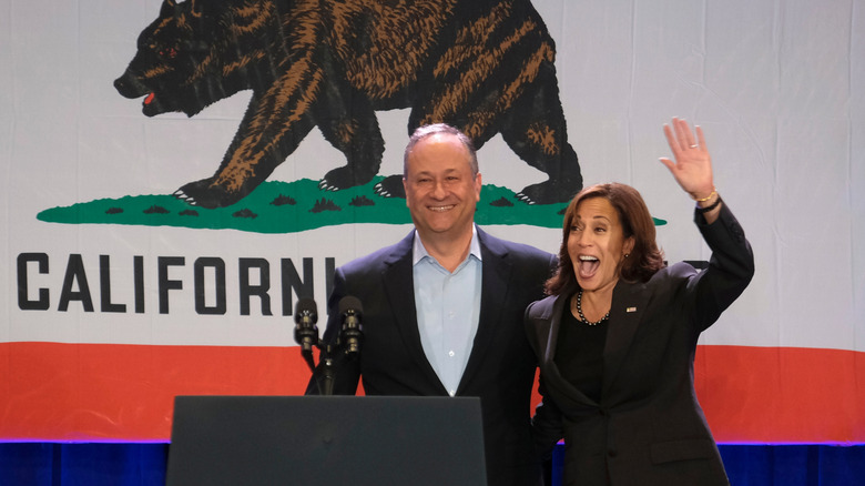 Standing in front the Californian flag, Doug Emhoff and Kamala Harris stand smiling behind a podium