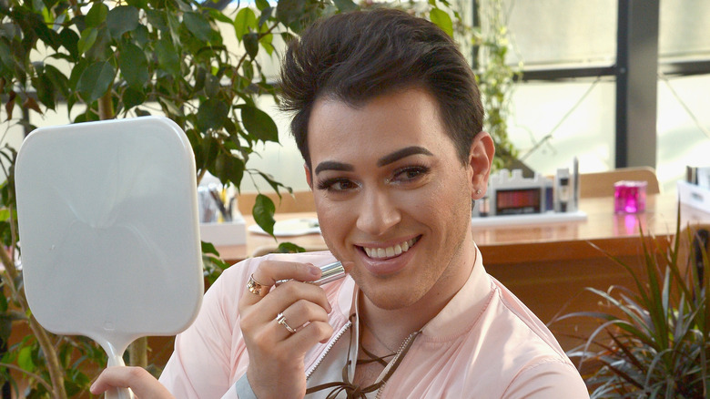 Manny MUA posing with a mirror and lipstick