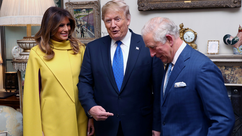 Melania and Donald Trump smiling next to King Charles III