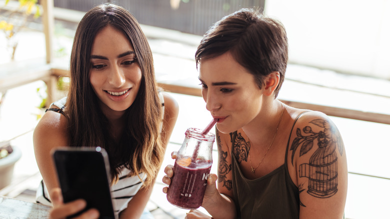 woman drinking while friend shows phone