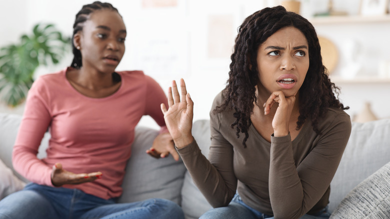 Two Black women on couch, one shutting out the other