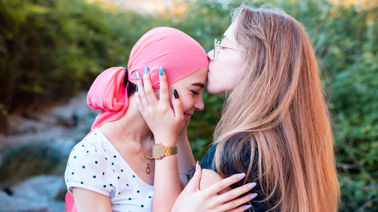 Young girl kissing a friend with cancer on the forehead