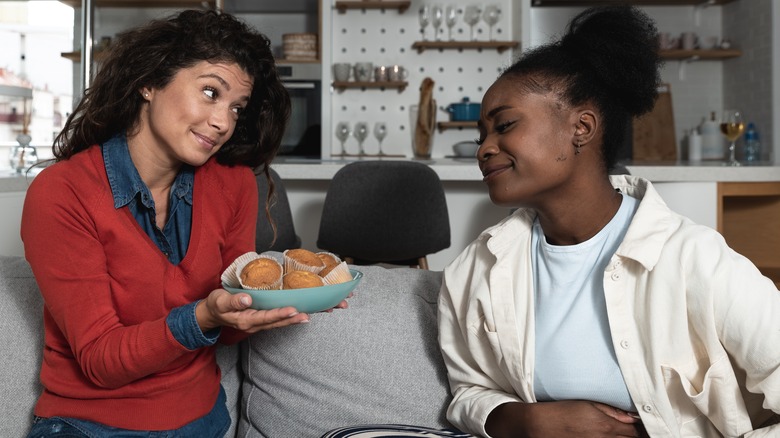 woman offering muffins to friend