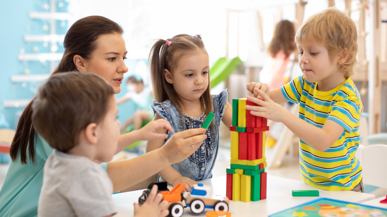 Preschool teacher and children play blocks