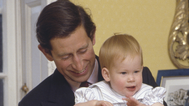 King Charles III smiling holding baby Prince Harry 