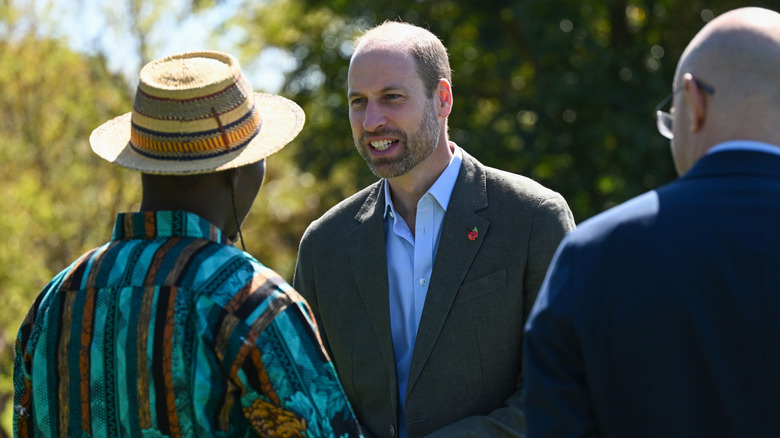 Prince William shaking hands with a man in a hat as another man looks on