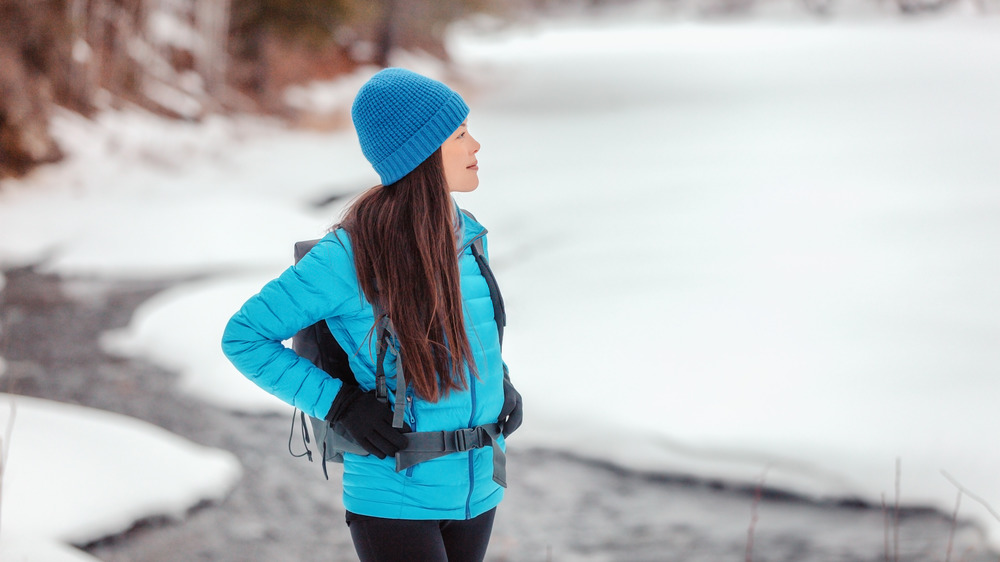 Woman hiking in winter wearing blue hat, coat, and black gloves