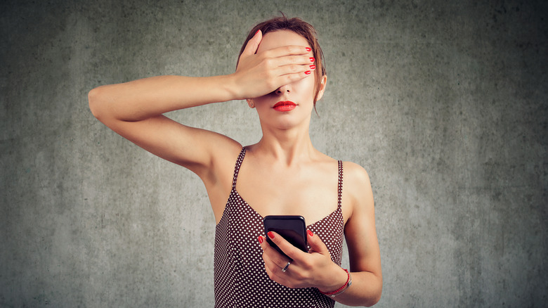 Woman covering eyes, holding phone