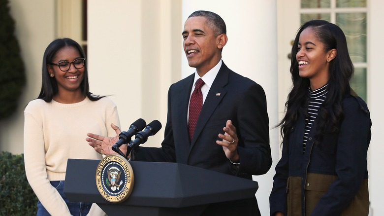 Sasha, Barack, and Malia Obama standing at podium