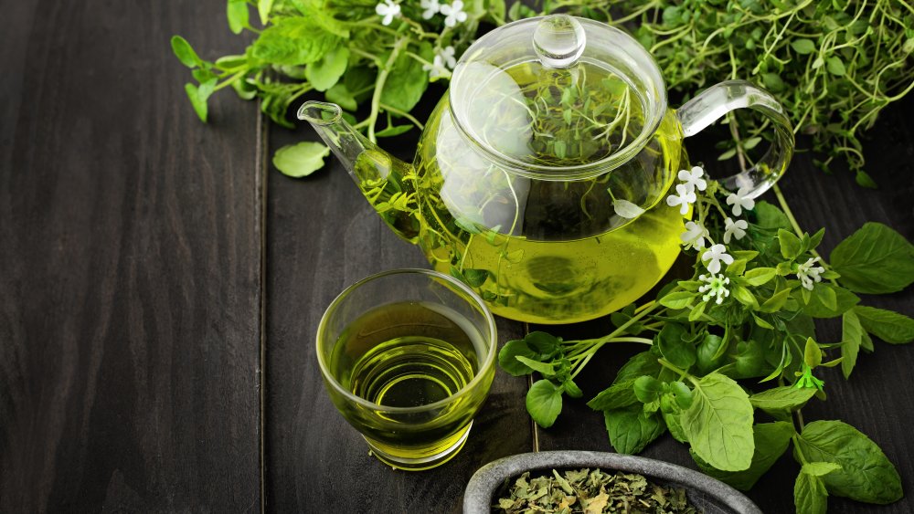 A pot and glass of green tea, with leaves and flowers