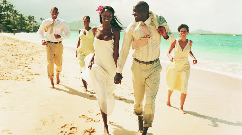 happy wedding party running along beach