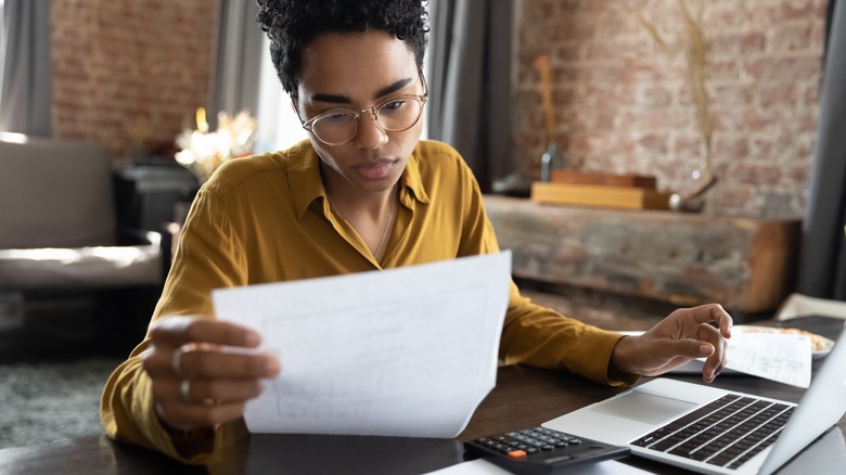 Woman with glasses, computer, calculator looking at paper