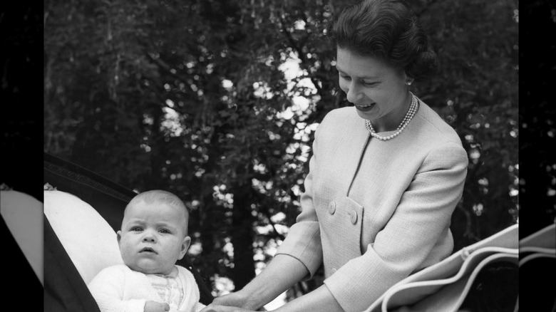 Queen Elizabeth smiling as she tucks baby Prince Andrew into his carriage