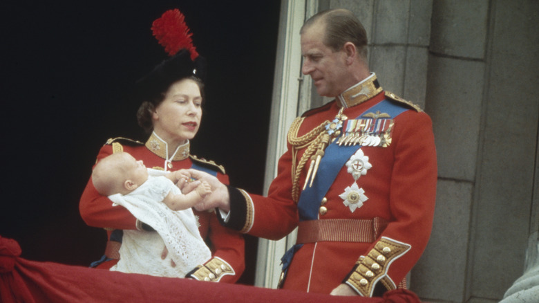 Prince Philip smiling and holding baby Prince Edward's hand while Queen Elizabeth looks on