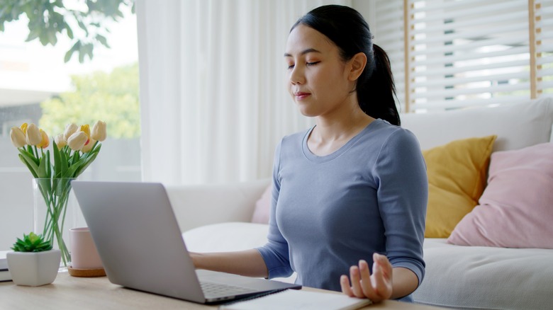 A woman meditating in front of a computer. 