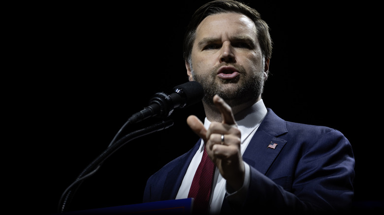 J.D. Vance delivering a speech in a suit with a red tie and American flag pin