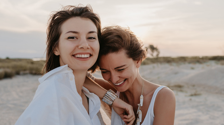 two women smiling and embracing at beach