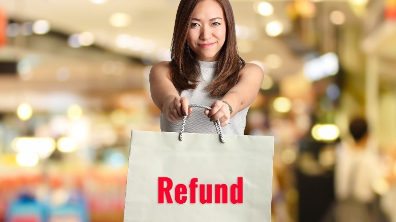 Woman holds a shopping bad that says "refund" in red text