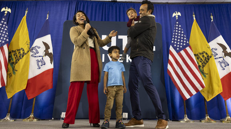 Apoorva Ramaswamy speaks into microphone next to son and Vivek Ramaswamy, holding younger son