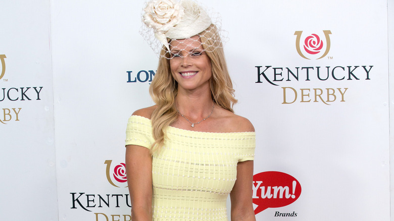 Elin Nordegren smiling in a light yellow dress, with a small white fascinator hat and matching short veil