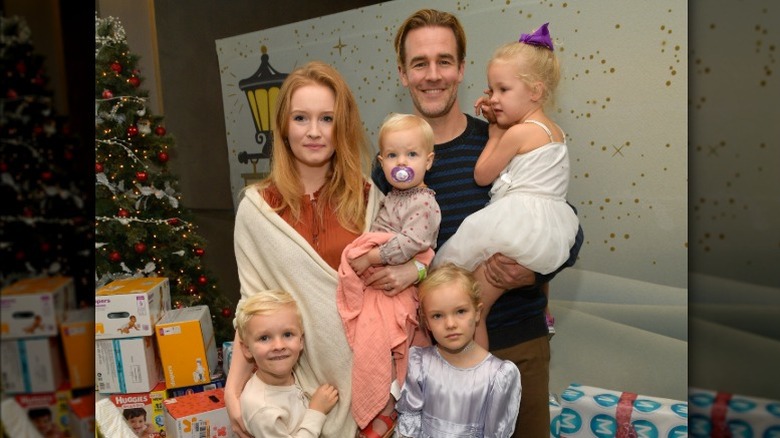 James Van Der Beek posing with his wife and 4 kids in front of Christmas presents