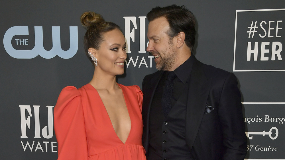 Actors Jason Sudeikis and Olivia Wilde formally dressed up and smiling at each other 