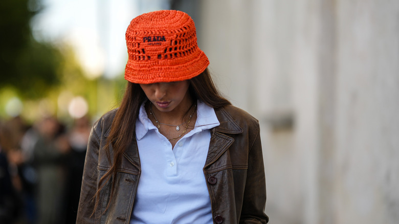 woman wearing white polo top, orange bucket hat, leather jacket