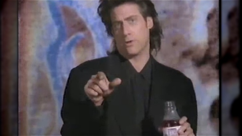 Richard Lewis speaking, pointing to camera and holding BoKu glass bottle