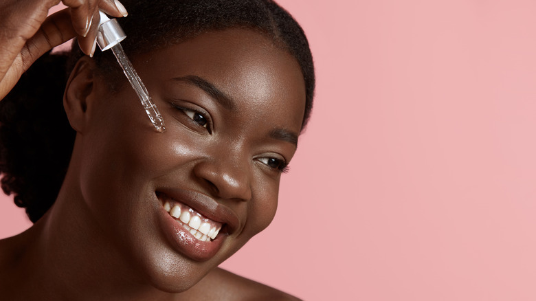 Black woman applying skincare serum to cheek with dropper