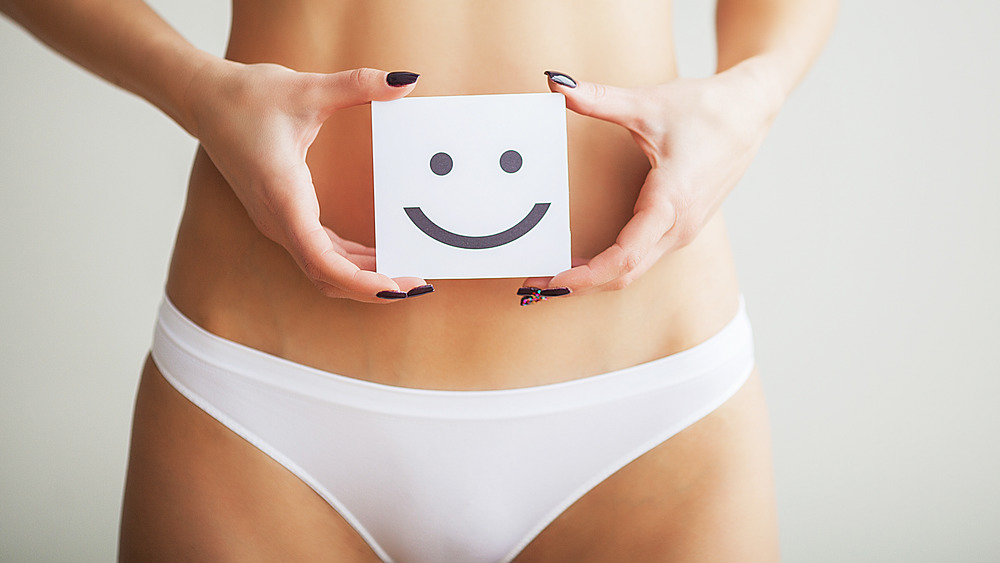 A woman in white underwear holding a smiley face over her abdomen 