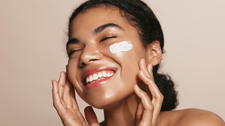 Woman smiling and touching face with skincare product