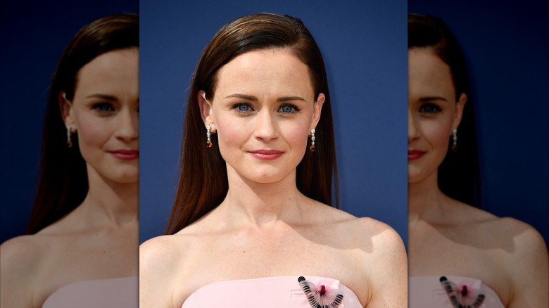 Alexis Bledel smiling thinly in front of a blue screen.