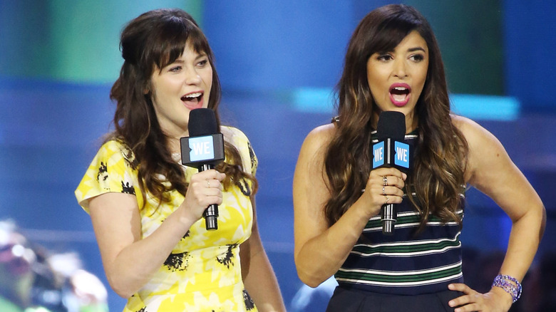 Hannah Simone and Zooey Deschanel talking into mics on stage