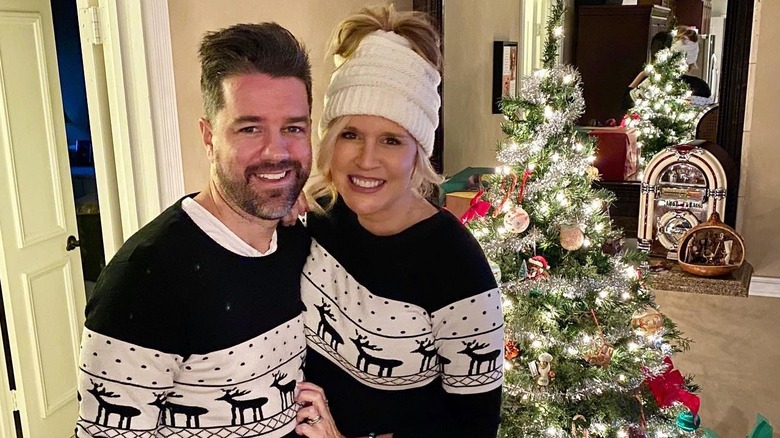 Paige Hemmis and her husband wear matching Christmas pajamas in front of a tree smiling.