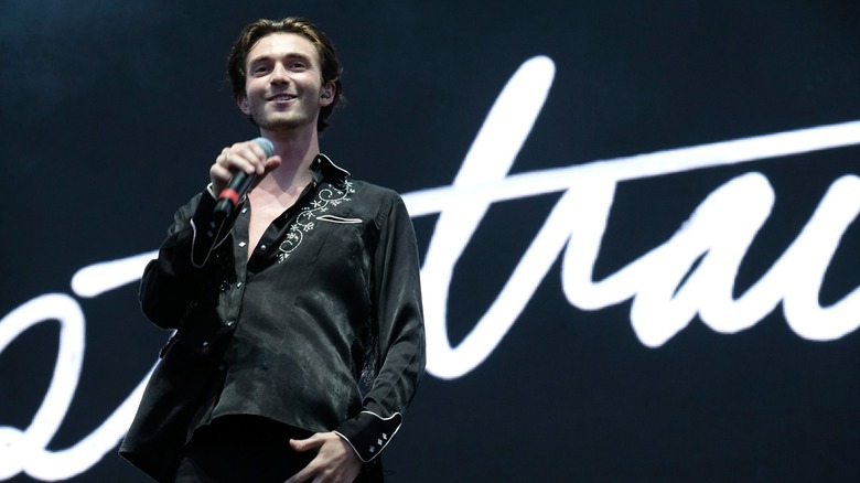 Greyson Chance holding a microphone in front of his Portraits album logo