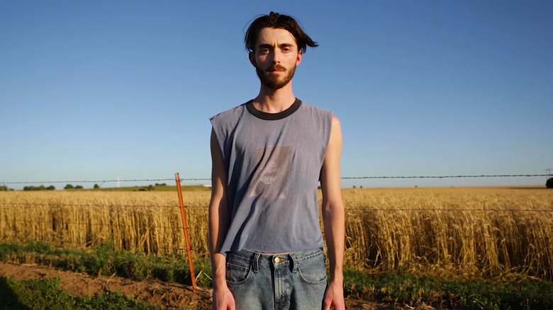 Greyson Chance in a tank top standing front of a wheat field