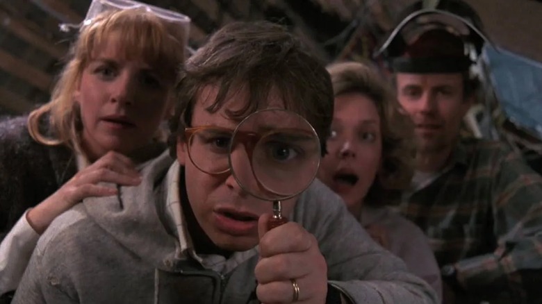 Wayne Szalinski looking through a magnifying glass, surrounded by the other parents, in Honey I Shrunk The Kids