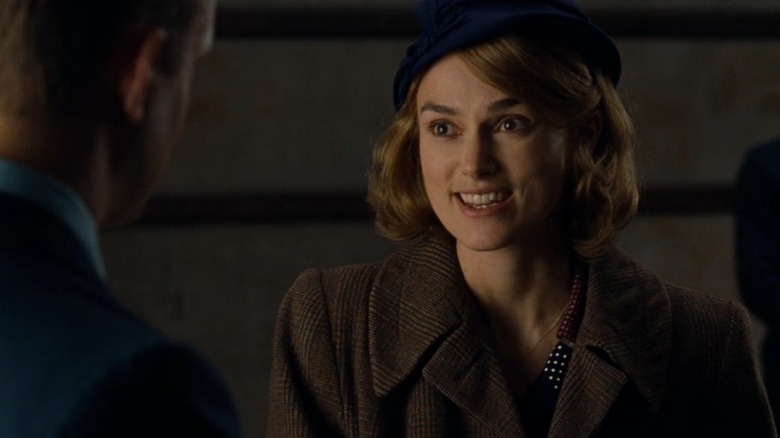 Keira Knightley with blonde hair and a brown coat, smiling in The Imitation Game