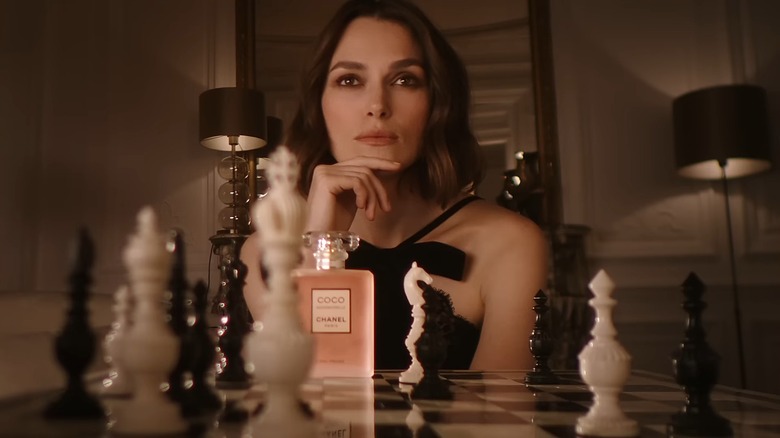 Keira Knightley sitting in front of a chess board with a pink bottle of Coco Chanel perfume, from the commercial