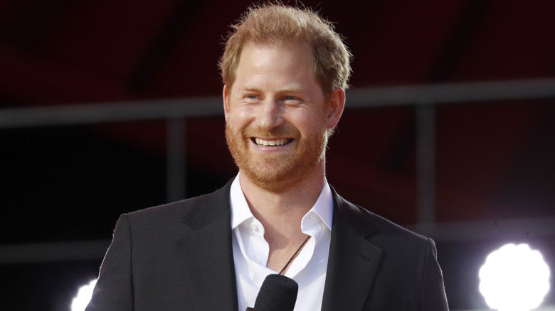 Prince Harry smiles while holding a microphone.