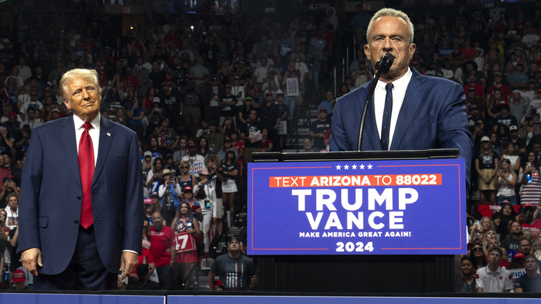 RFK Jr. speaking at podium Donald Trump background