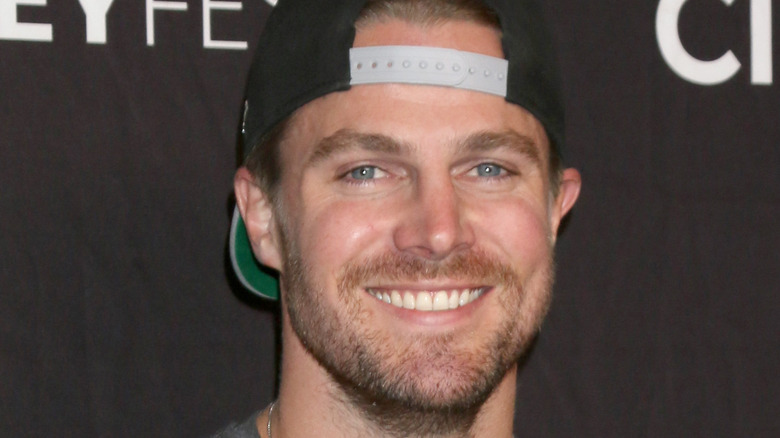 Stephen Amell grinning wearing backwards hat