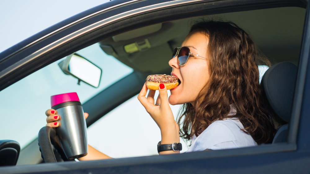 woman in car drinking coffee and eating a donut