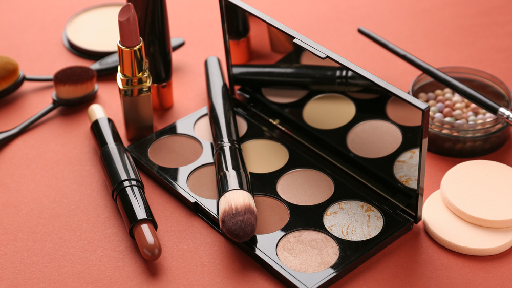 A contouring brush lays on a pallet next to other cosmetics.